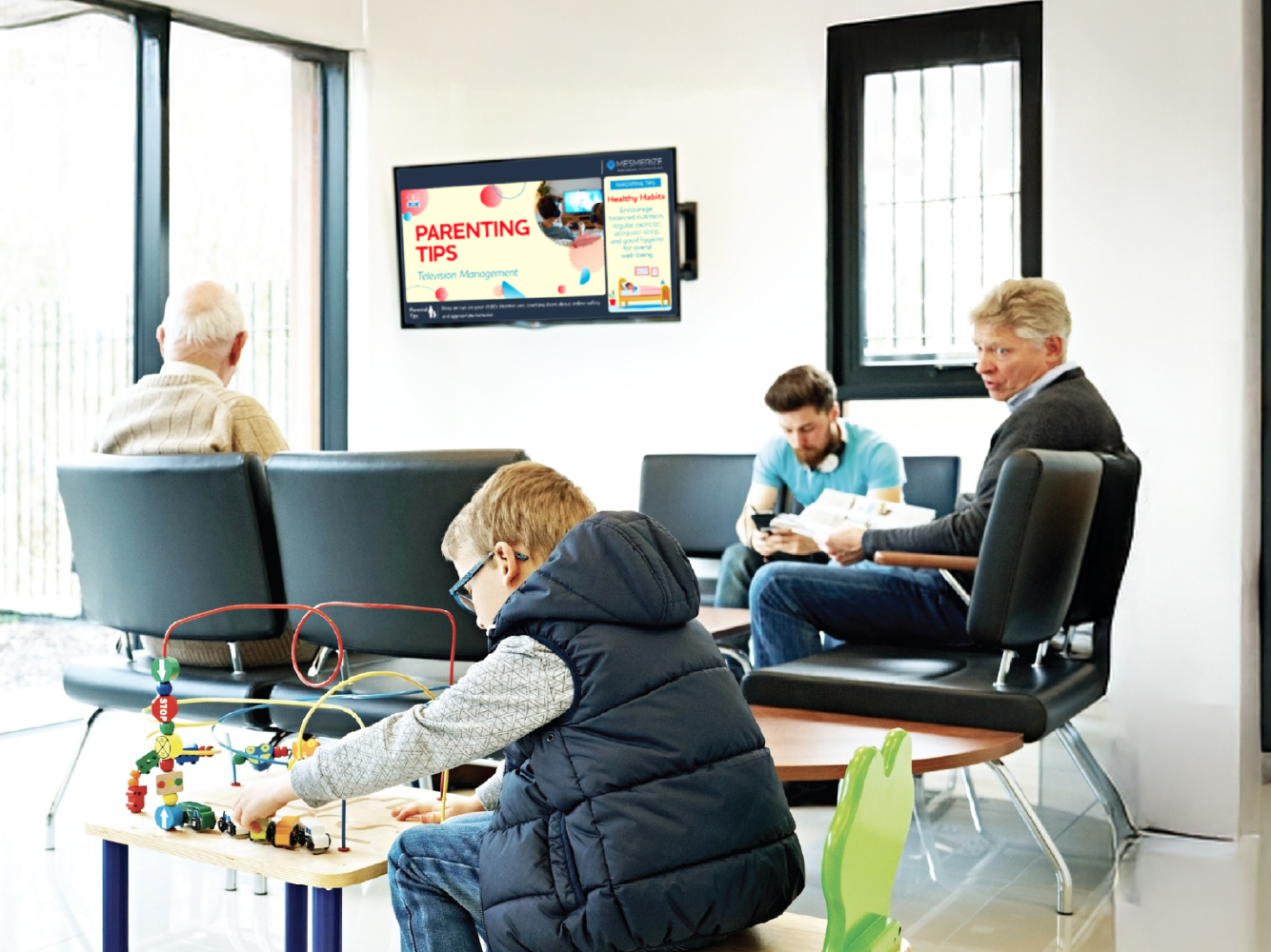 Kid playing with toys in waiting room, as patients read info displayed in a digital screen on the wall.